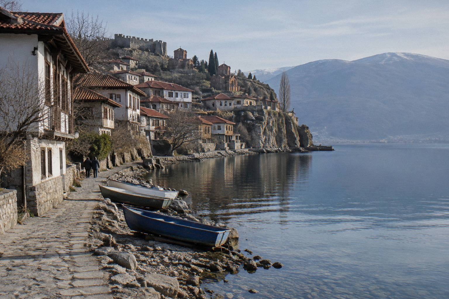 Red tile roofs of a lakeside old town stepping down a hillside to a rocky shore and calm clear lake in soft morning light