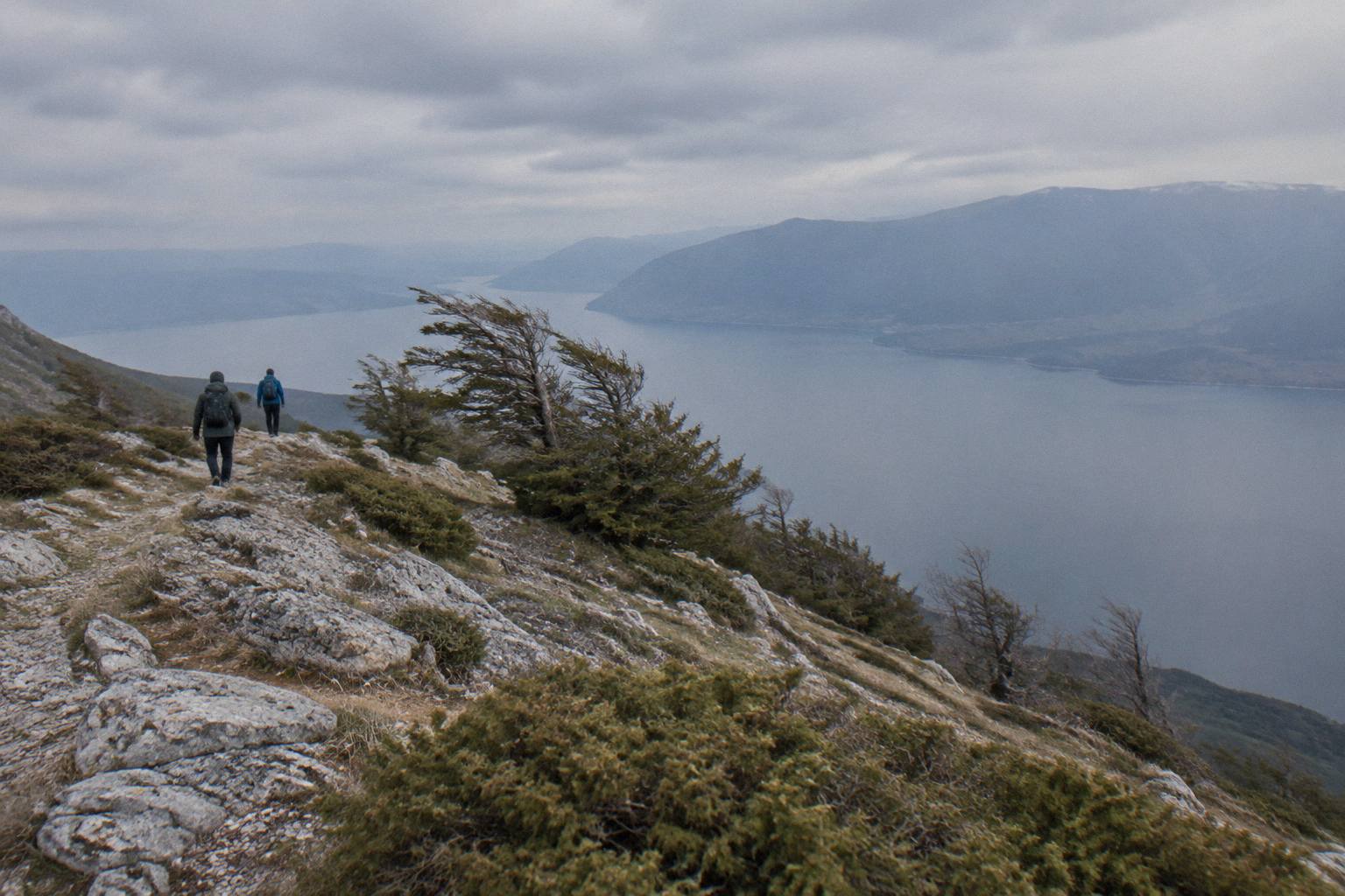 An open mountain ridge of pale grey rock and low scrub with a freshwater lake far below in haze