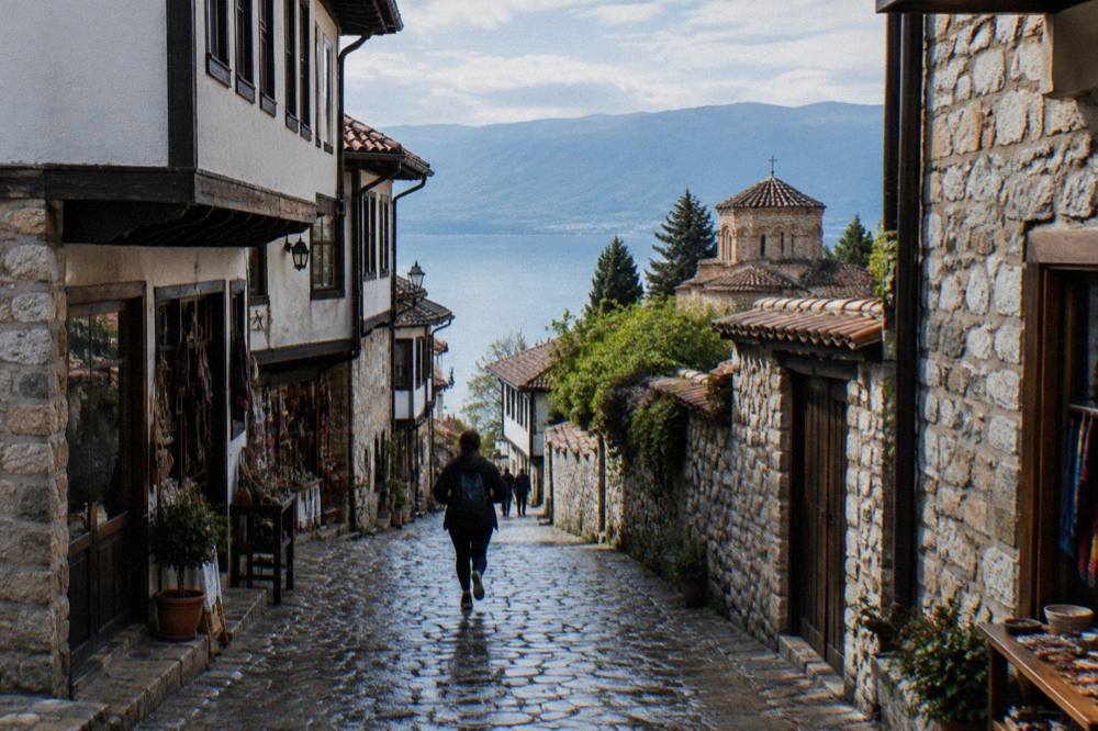 A narrow stone lane in Ohrid old town with small shop fronts and the lake visible beyond
