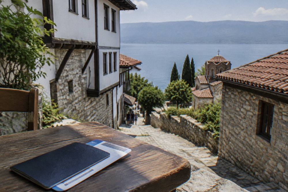 A passport and boarding pass resting on a wooden table beside a lake view