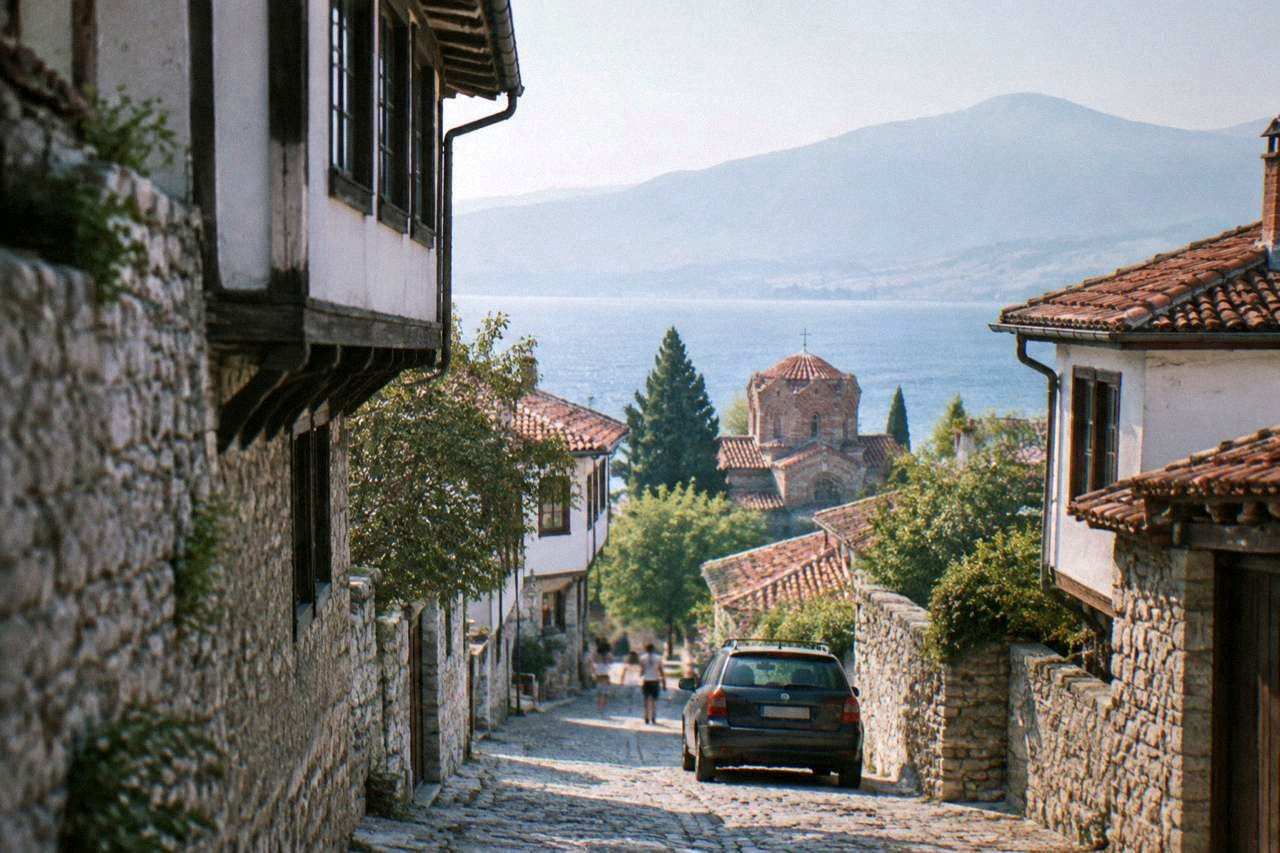 A narrow stone street in Ohrid old town with a parked car and lake light at the end of the lane
