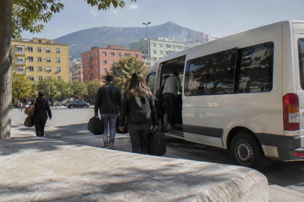 A parked minibus on a small town street with passengers loading bags