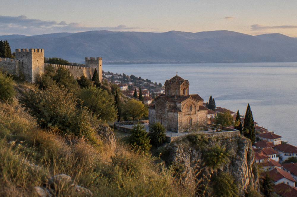 A stone church on a cliff above calm lake water at dusk
