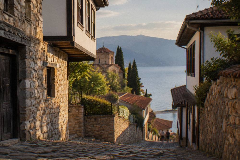 A pebble shoreline on the southern shore of Lake Ohrid with calm water and hills beyond