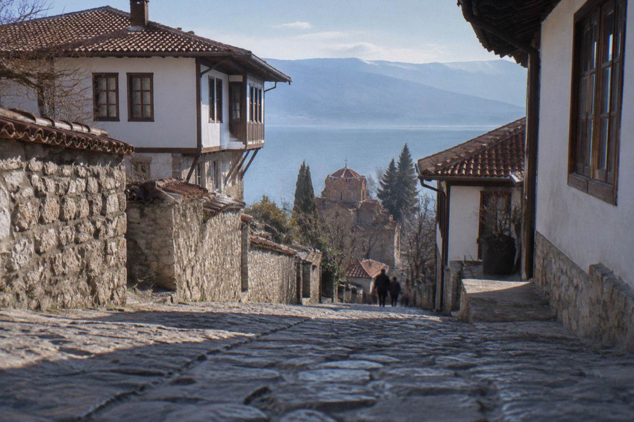 A lakeside town rising from the shore of a blue mountain lake toward a hilltop fortress