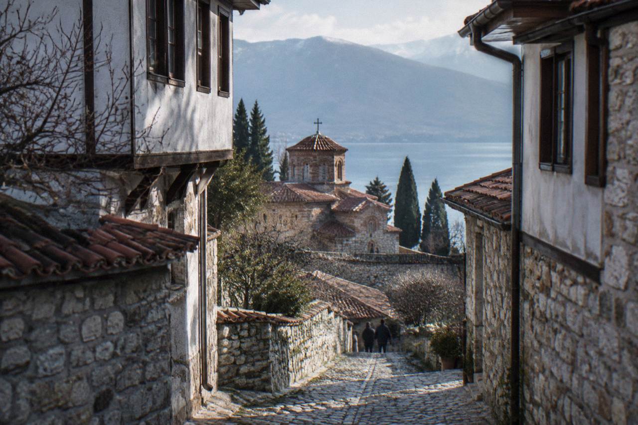 Stone church above the shore of a blue mountain lake with a walled old town behind