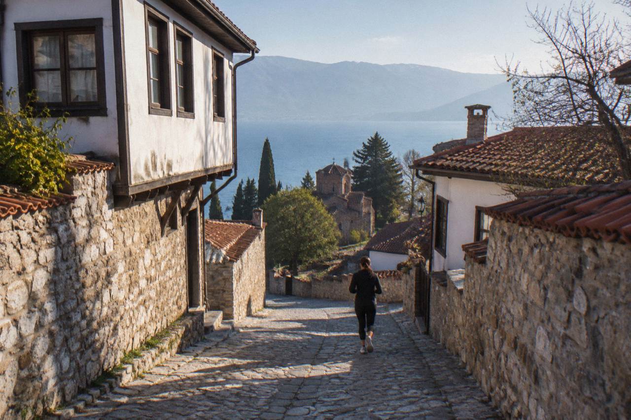 A mountain road winding toward the blue water of Lake Ohrid with hills on the horizon