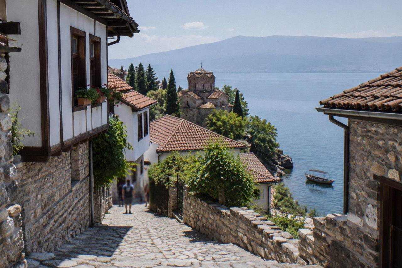 A wooden boat on clear blue water below a hillside monastery on Lake Ohrid