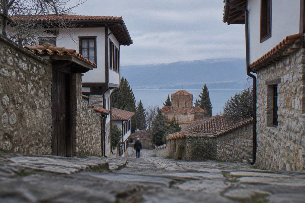 A stone church with a red tile roof standing above the blue water of Lake Ohrid
