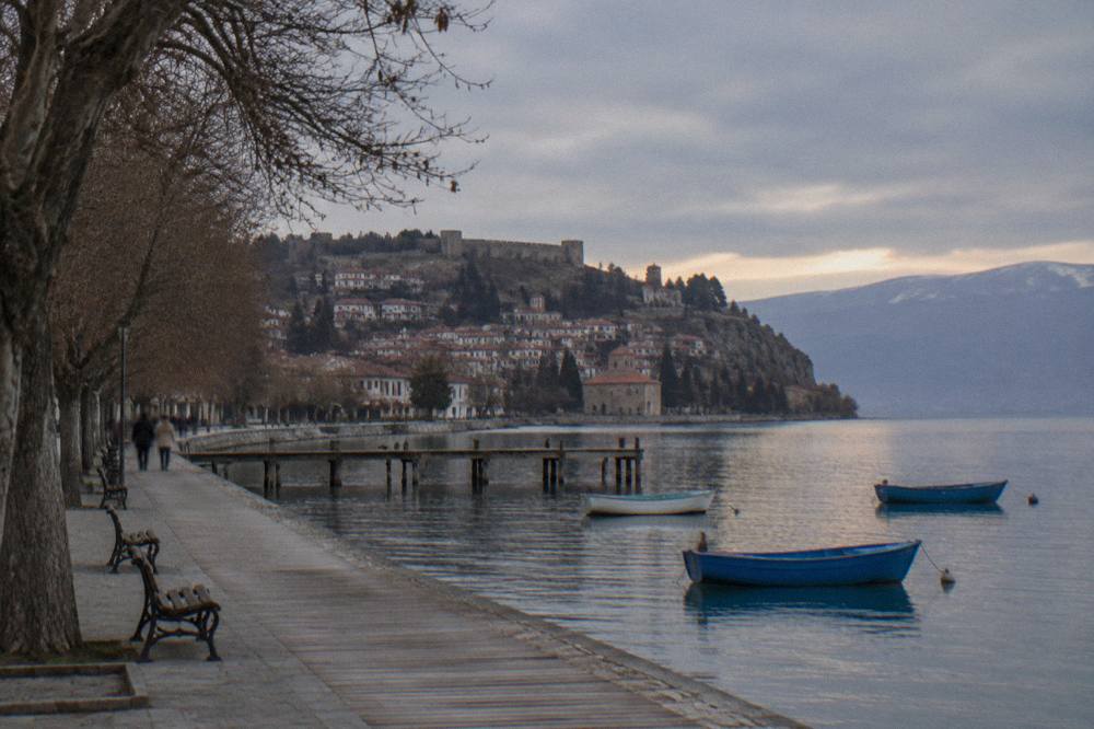 Rowing boats and a lakeside promenade in Ohrid at sunset with the old town behind