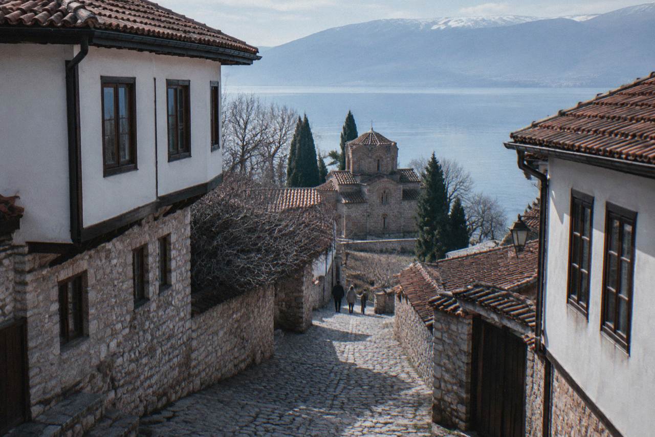 Stone church above the shoreline of a clear mountain lake with a walled old town rising behind it