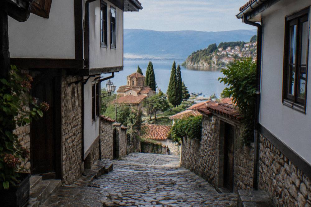 Small boats moored along a lakeside quay with a hillside town of red roofs behind them