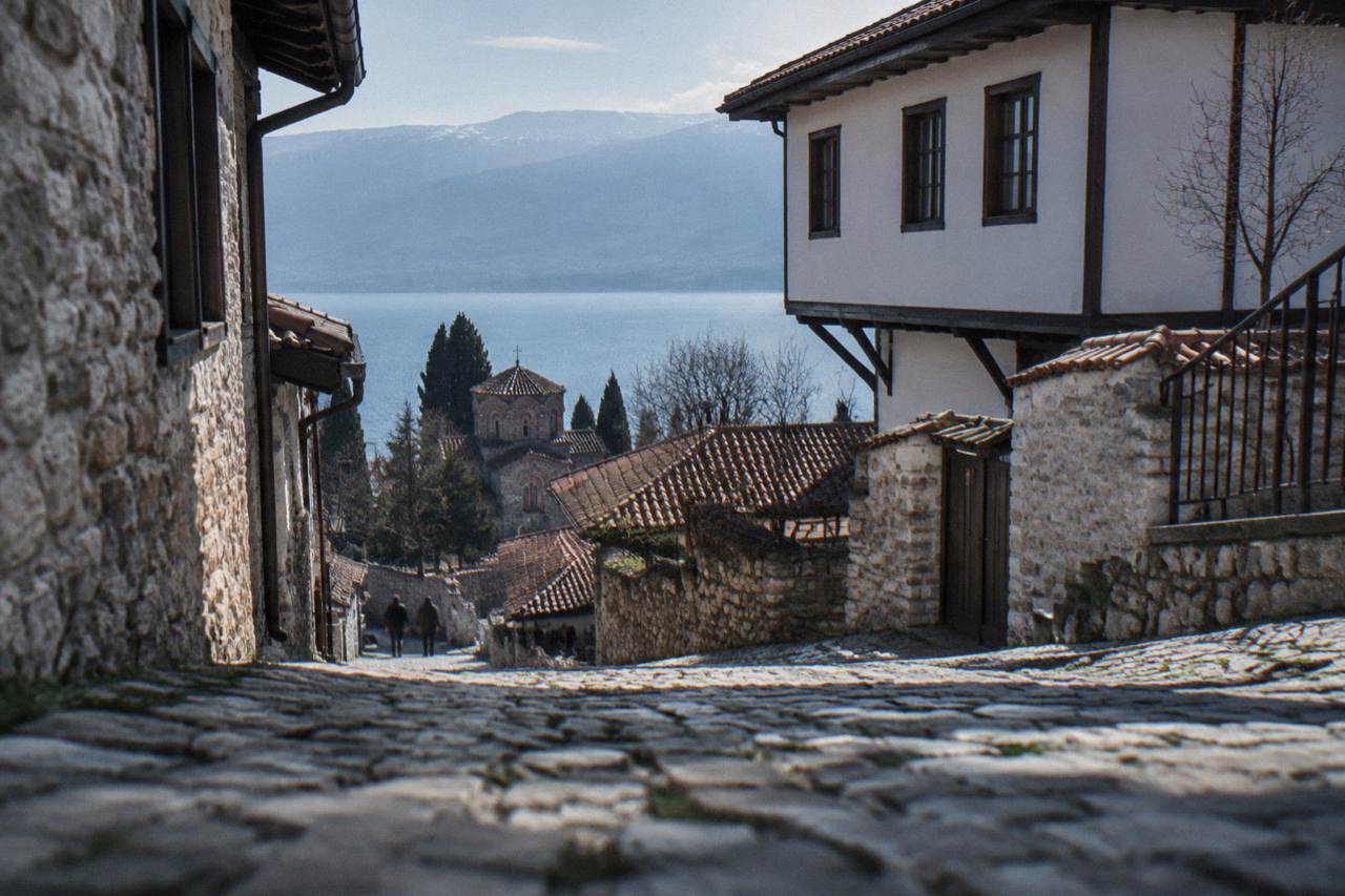Stone houses on a hillside lane rising from the shore of a blue mountain lake