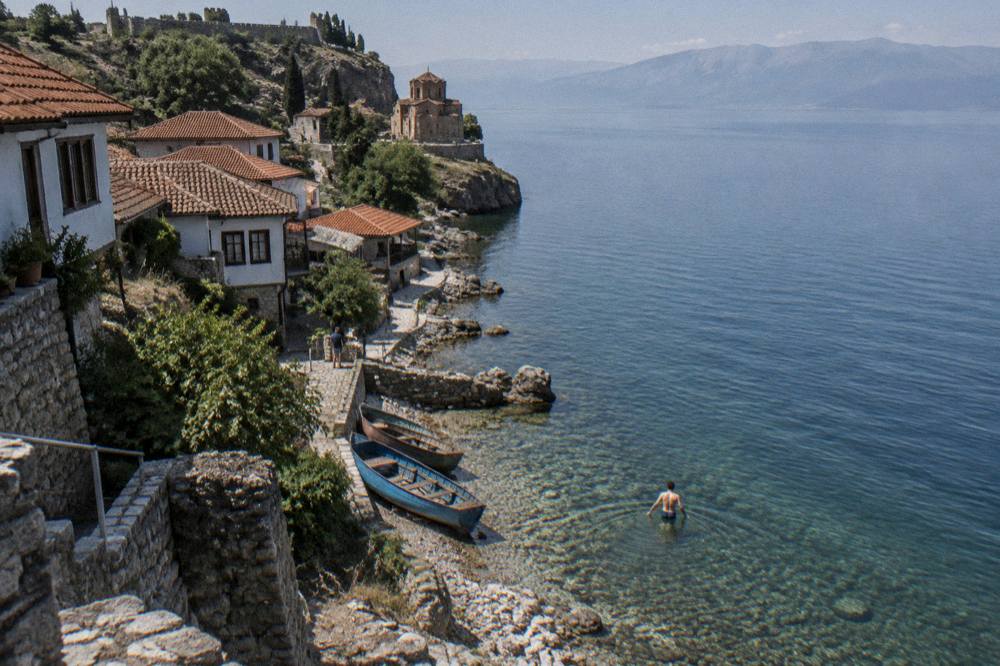 A swimmer entering the clear fresh water of Lake Ohrid from the shore below the Kaneo district