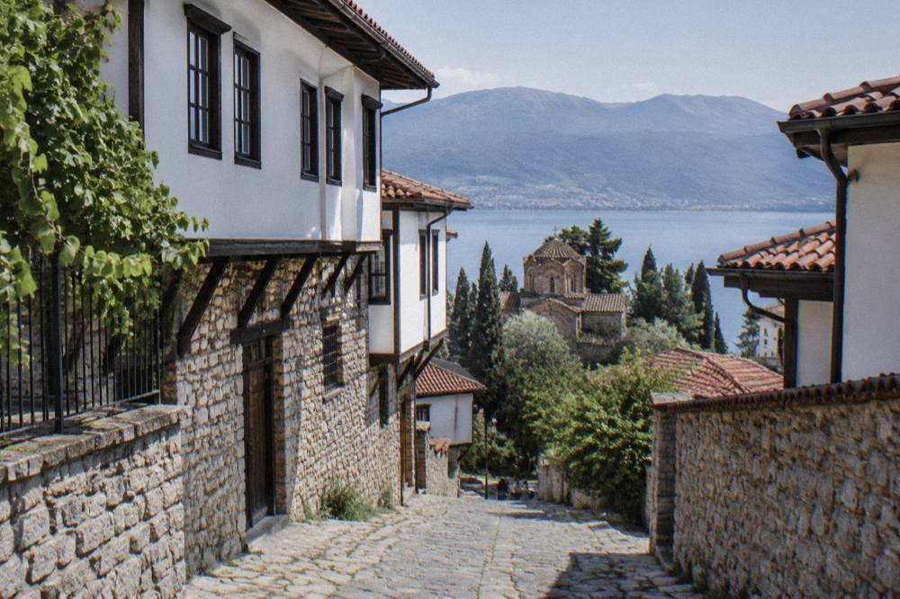 A village of houses among trees above a bay on Lake Ohrid with mountains behind