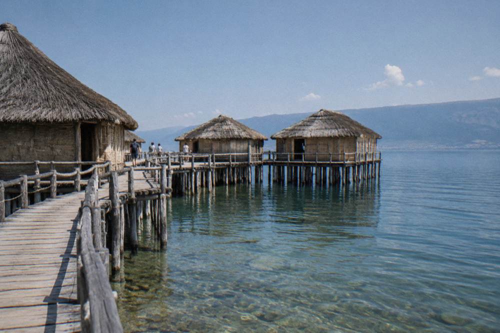 A reconstructed pile-dwelling museum standing on wooden platforms over the clear water of a lake bay