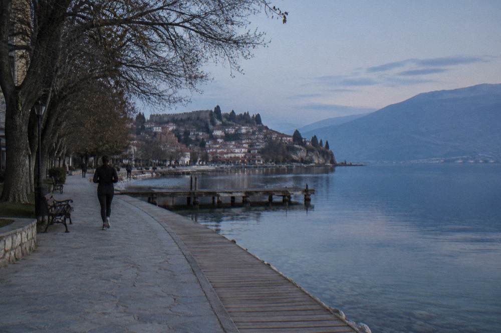 A wooden lakeside promenade curving along clear shallow water toward a small harbour