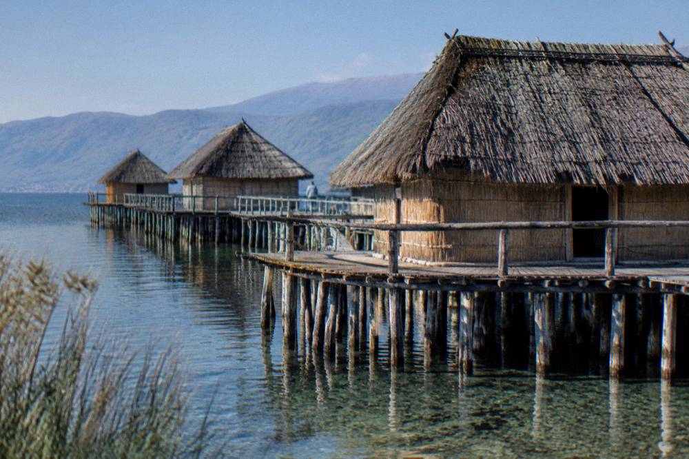 A reconstructed prehistoric pile dwelling standing on stilts in a quiet lake bay