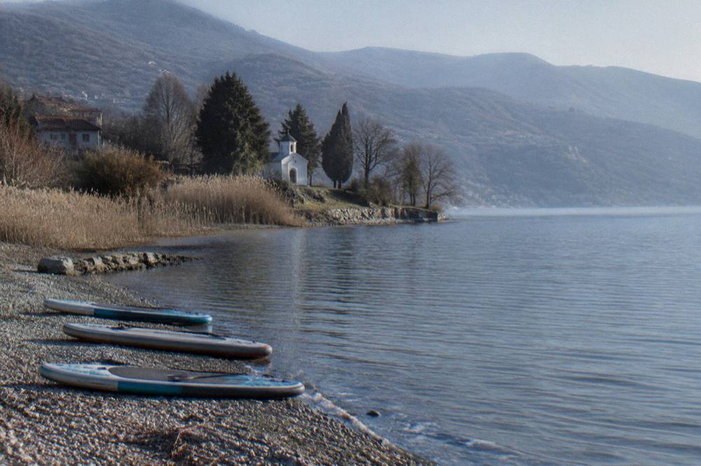 Paddleboards resting on a pebble beach with lake water lapping at their edges
