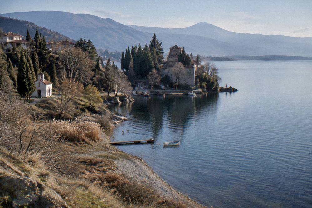 A monastery among trees at the water's edge with springs and boats near the shore