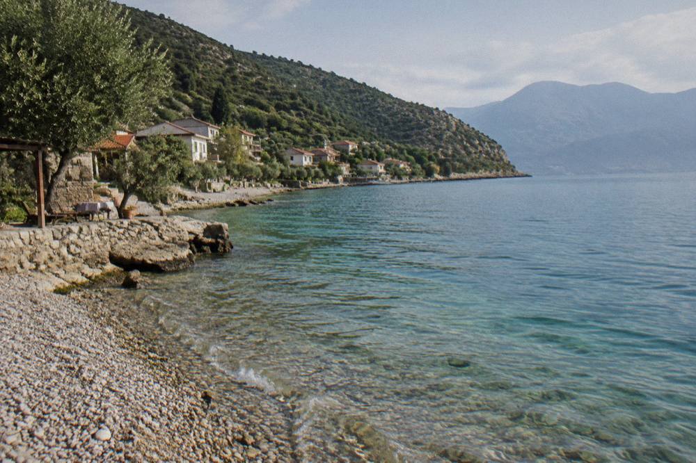 Turquoise water lapping a narrow pebble shoreline with wooded hills rising behind