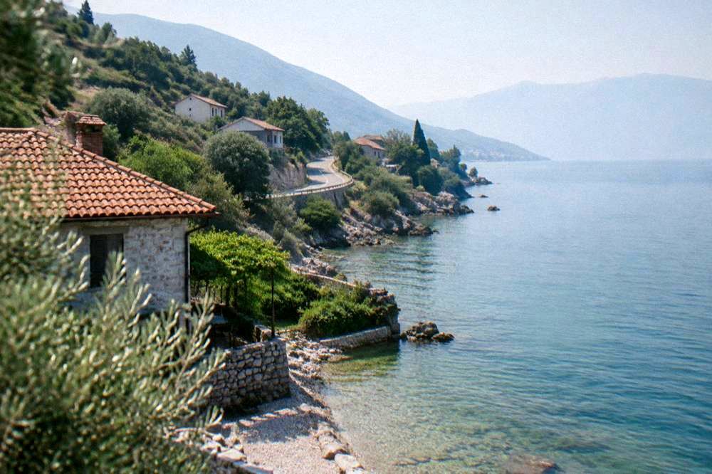 A narrow road winding along a wooded shoreline above the blue water of the lake