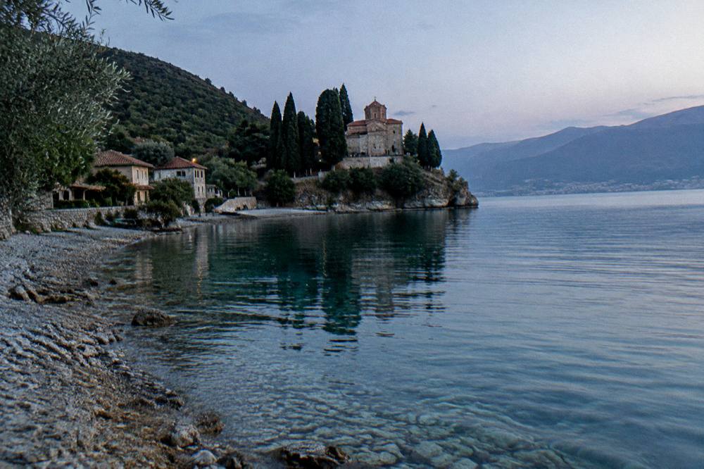 A monastery building among trees close to the shore at the southern end of a lake