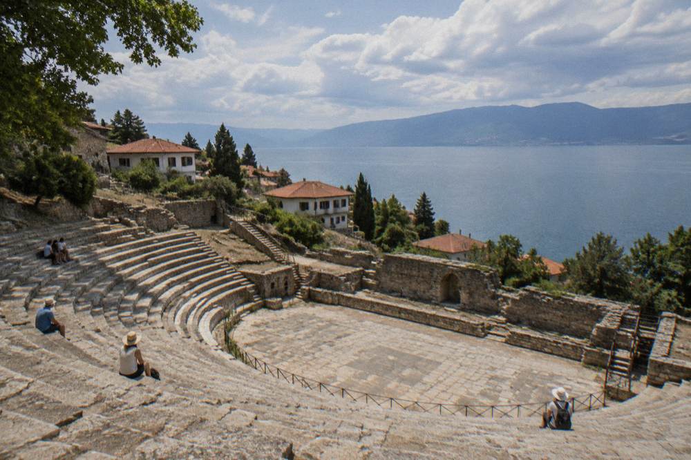 Wide view over ancient theatre seating tiers with Lake Ohrid and hills visible in the distance