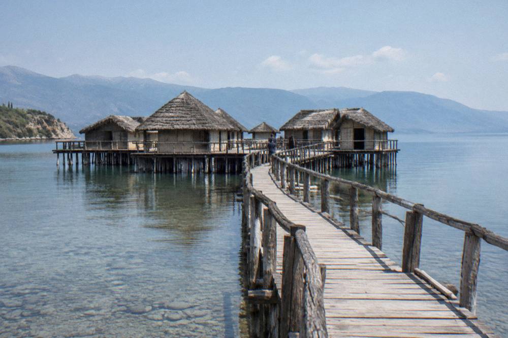 A wooden walkway leading over the shallows of the bay toward the reconstructed dwellings