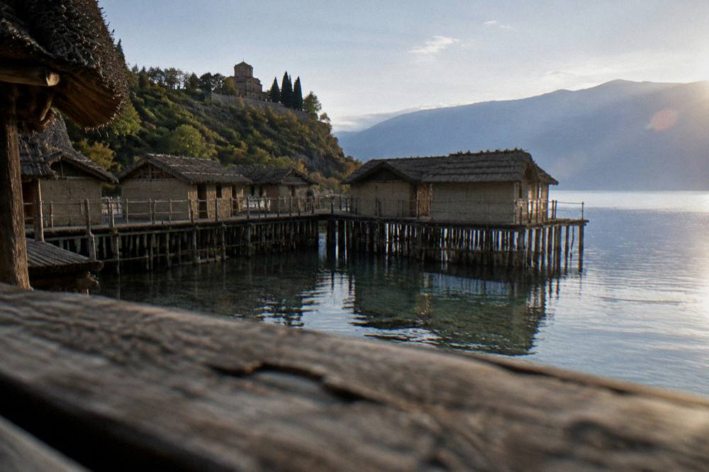 A hillside monastery among trees above the shoreline of a blue mountain lake
