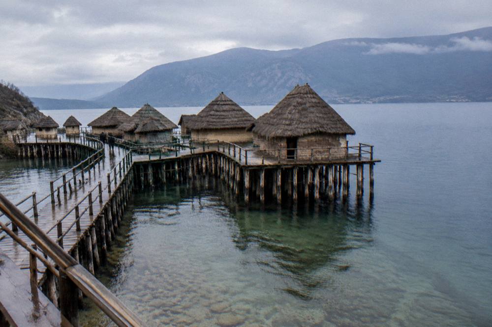 A wooden platform walkway over a quiet bay with mountains rising behind the far shore