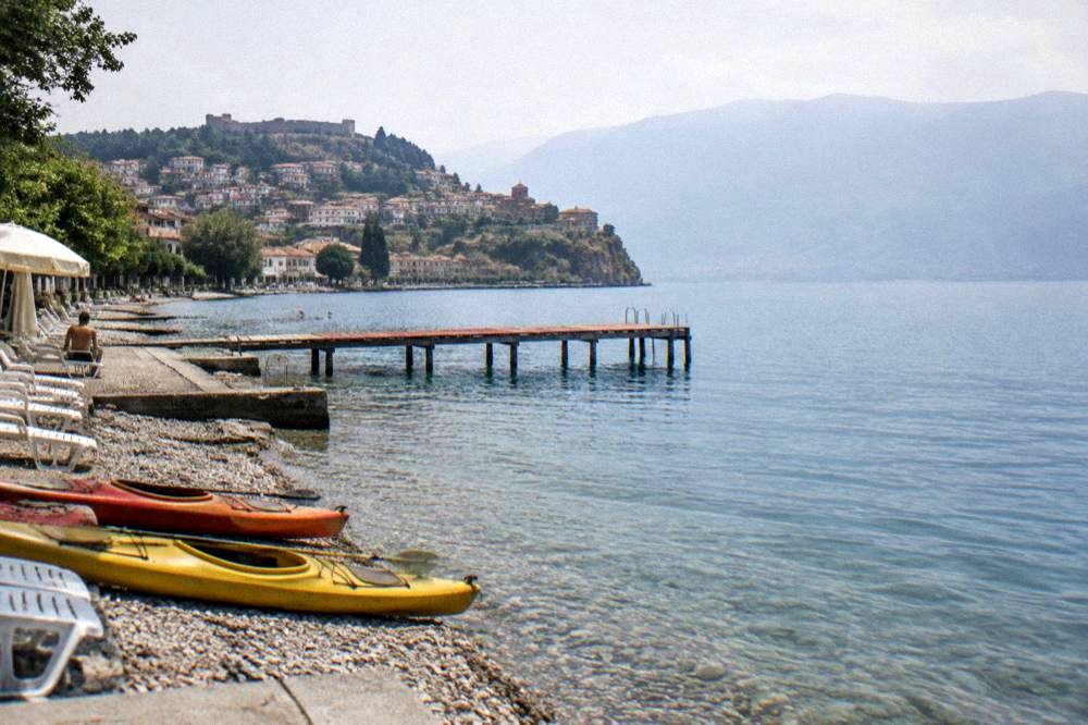 Kayaks pulled up on a pebble beach beside turquoise lake water