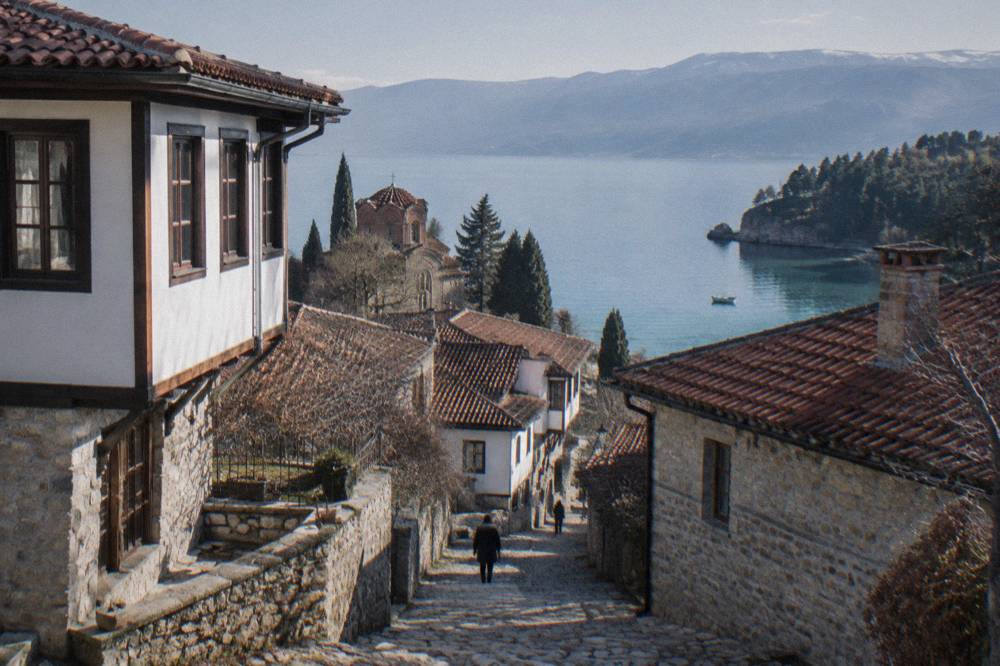 A small boat on clear green water near a wooded shoreline of Lake Ohrid