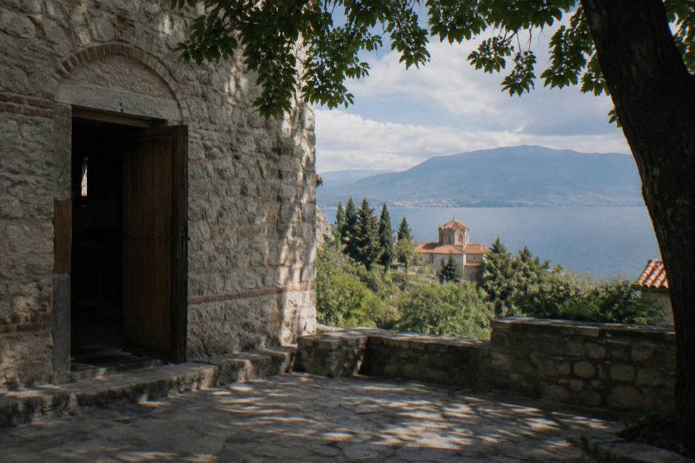 A hillside church with a red roof seen through trees above a blue lake