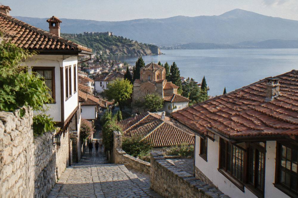 A wide view of Ohrid old town rooftops descending to a calm lake at golden hour