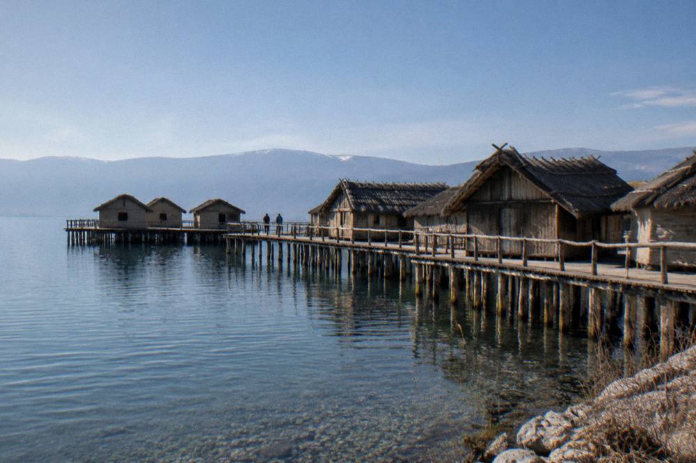 Reconstructed wooden pile dwellings standing on stilts above a blue mountain lake
