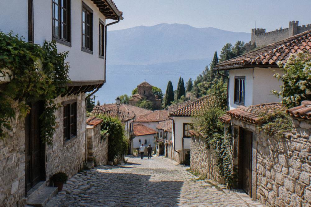 The stone lanes of Ohrid old town climbing toward a fortress wall above the rooftops