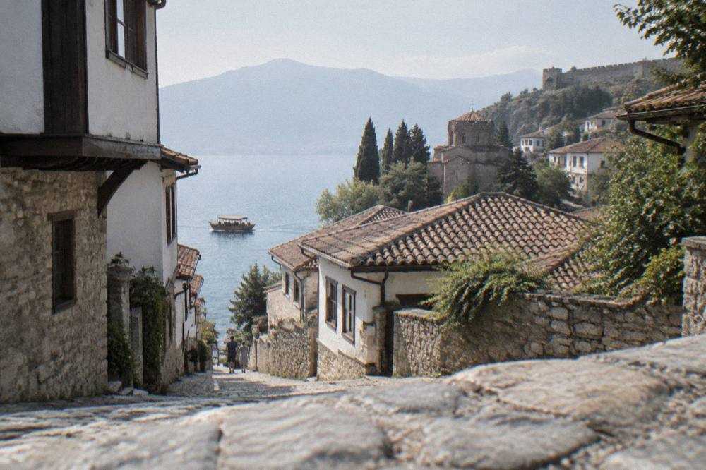 A wooden boat cruising along the Ohrid lakeshore with the old town rising behind