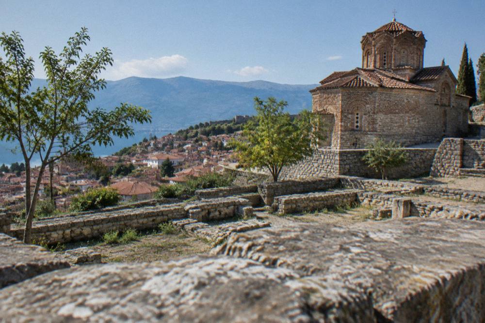 Walled terrace with cut stone foundations of ancient buildings below a modern church facade on a hillside