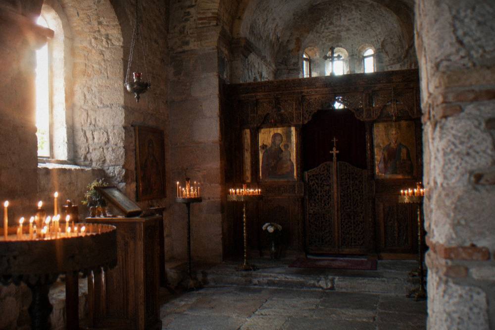 Interior of a stone church with candle stands and a carved wooden screen in front of an altar