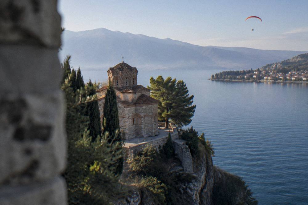 A paraglider wing high above a lake shore with a small town at the water's edge