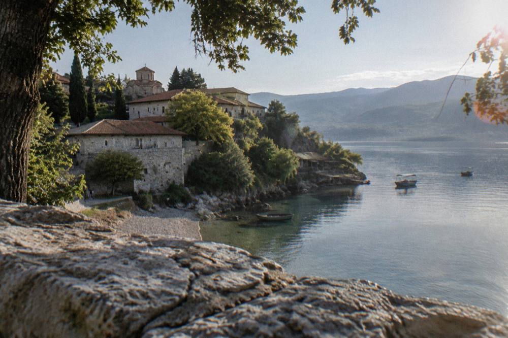 A lakeside village with a pebble beach and calm water below wooded hills