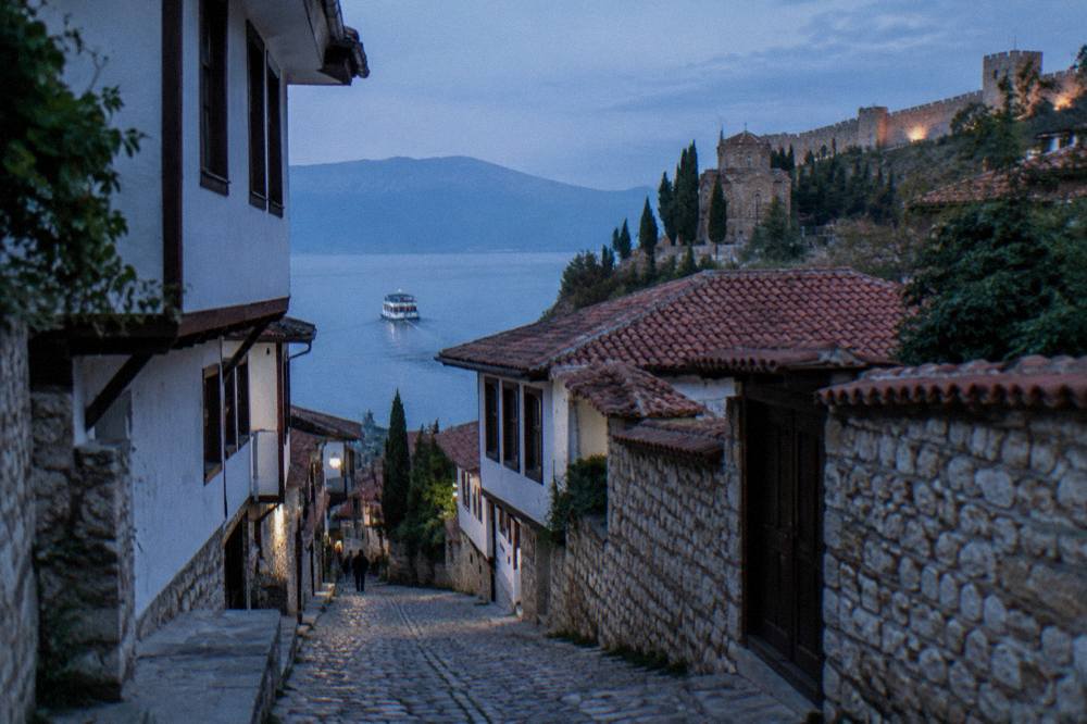 A touring boat leaving a harbour with a walled old town on a hillside behind