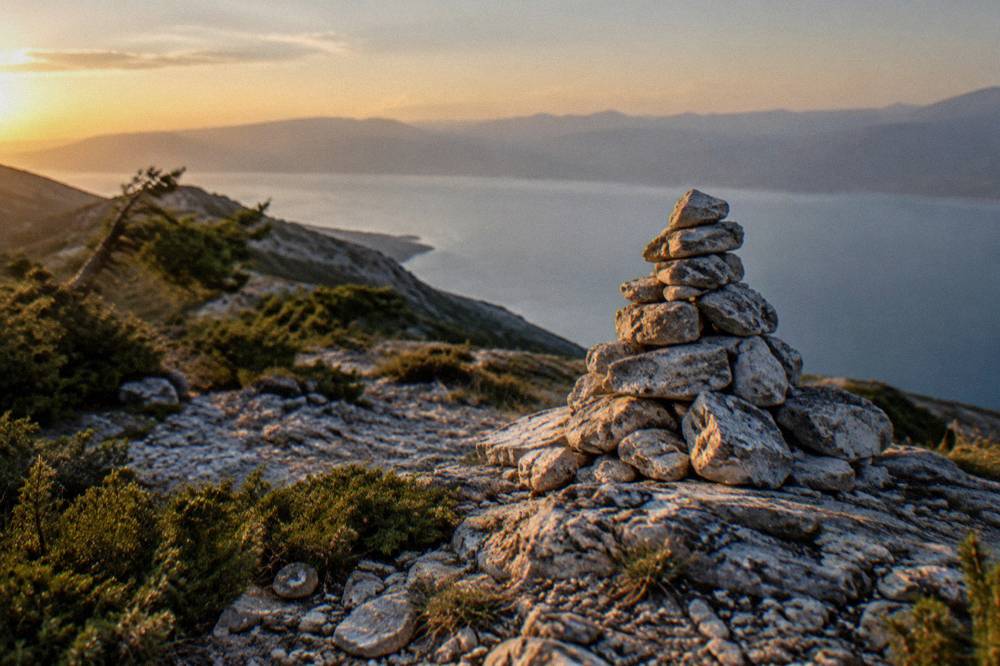 A stone cairn on a bare mountain pass with a wide view over a calm lake