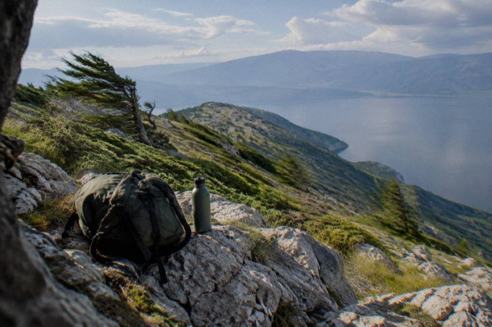 A backpack resting on a rock beside a water bottle with mountains in the background