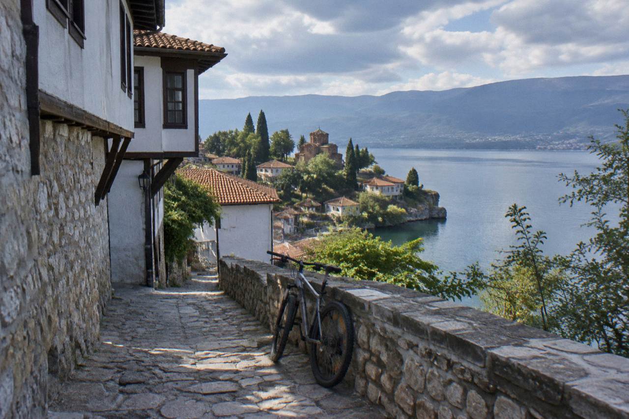 A bicycle parked on a lakeside path with the old town of Ohrid and Lake Ohrid behind it