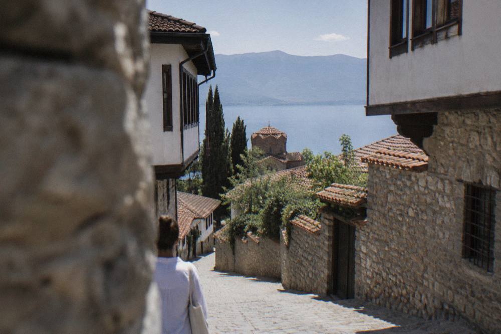 An empty shore road beside Lake Ohrid with wooded hills rising from the water