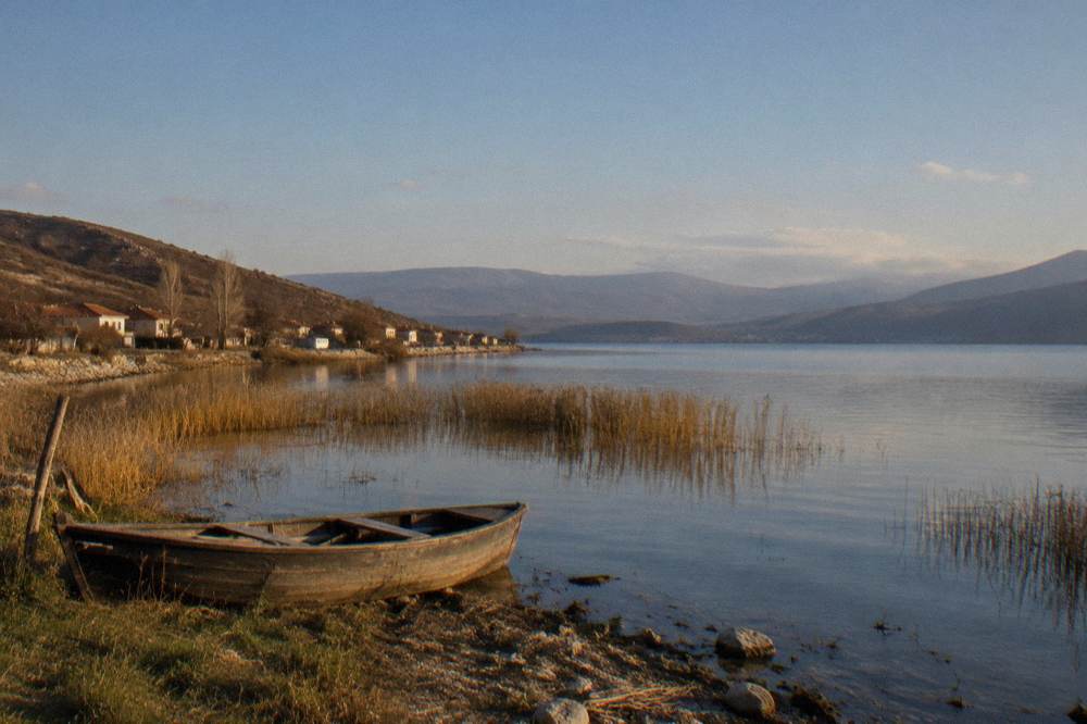 A small lakeside village with low houses and a stony shoreline under hills