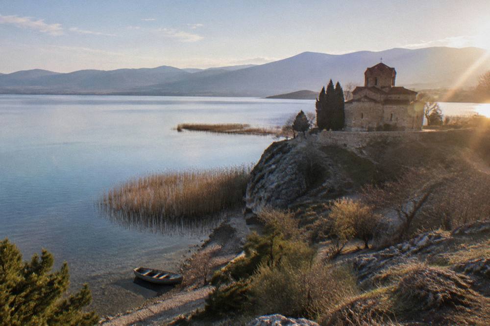 A stone church on a rocky point above a clear lake at golden hour