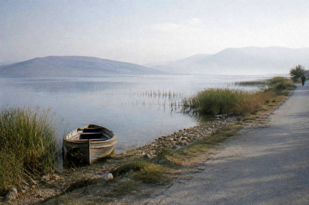 An empty shoreline road beside a wide still lake in early morning light